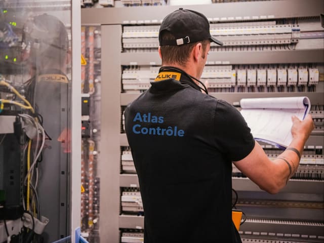 Inspecteur Atlas Contrôle consultant les schémas de l'installation devant un tableau électrique lors d'un contrôle